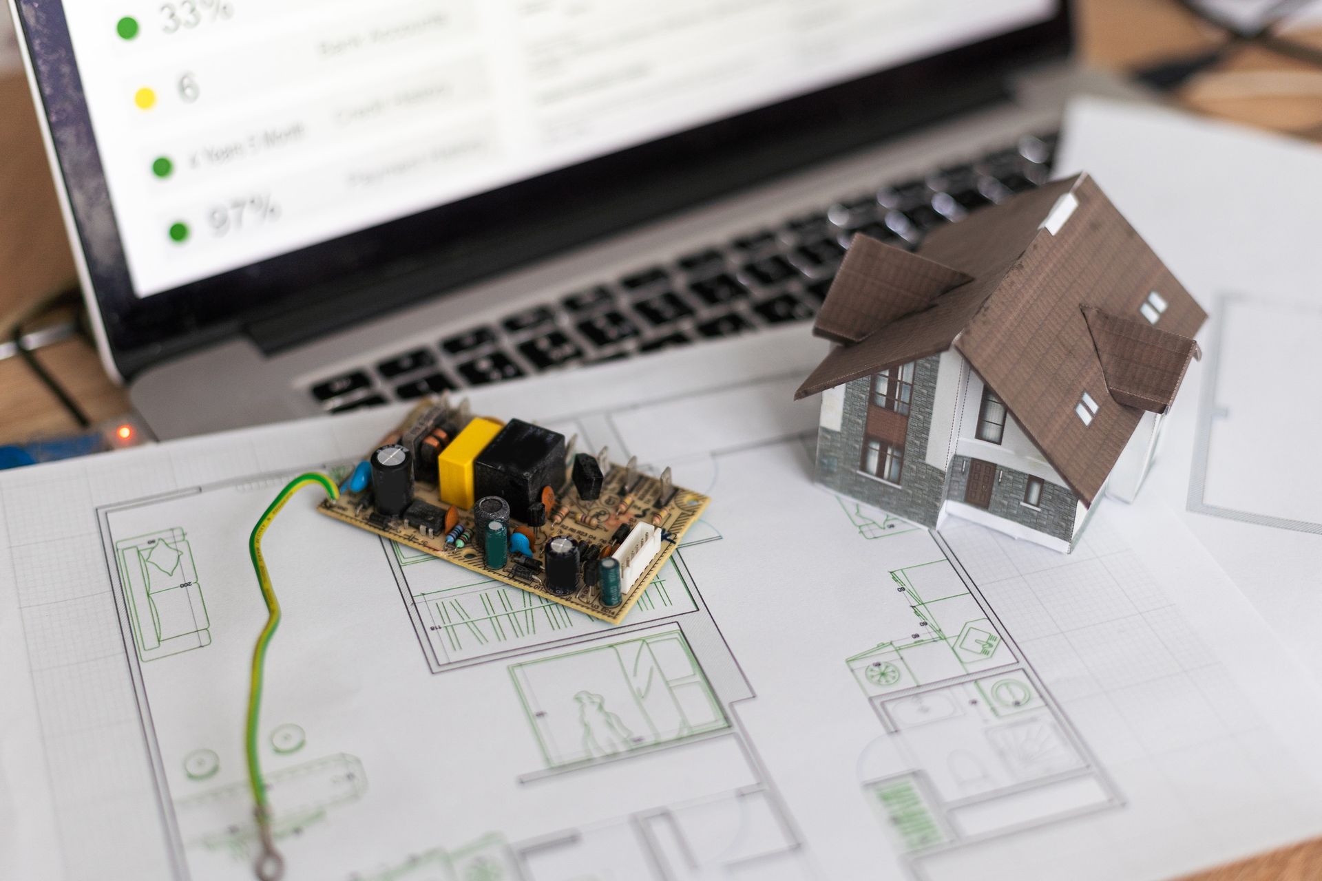 Portátil, maqueta de casa y planos sobre un escritorio